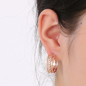 Gros plan d'une boucle d'oreille créole en C ajourée or rose portée par un mannequin