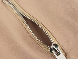 Dettaglio macro della cerniera in metallo su pantaloncini kaki con trama del tessuto fine