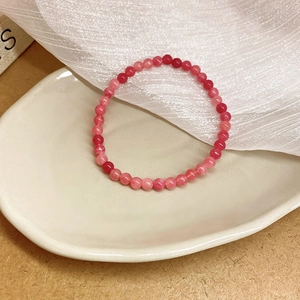 Detailansicht eines lebendigen Erdbeerquarz-Perlenarmbands auf einem Keramikteller