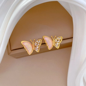 Detailed macro view of gold butterfly earrings with pink glaze and white zircons