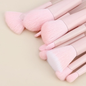 Dettaglio di 10 pennelli per trucco rosa con setole morbide su sfondo beige