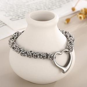 Detail view of silver heart pendant chain bracelet on a decorative white ceramic vase