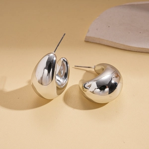 Macro detail of polished silver teardrop C-shape earrings on a minimalist stone base