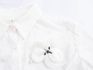 Close-up of white textured shirt collar featuring pearl button and 3D floral brooch detail