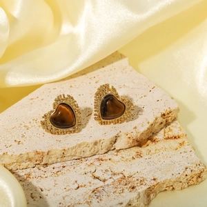 Vintage heart-shaped tiger eye stud earrings with gold serrated edges on silk background