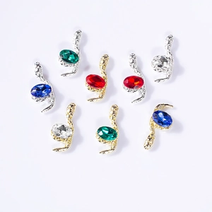 Macro detail of snake-shaped nail art charms with colorful gemstones in gold and silver