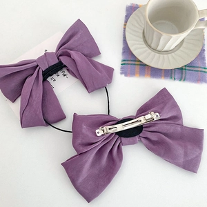 Satin purple bow hair tie and clip set on a white desktop with lifestyle props
