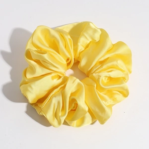 Close-up of yellow satin scrunchie showing glossy silk texture and elegant pleats