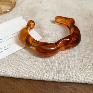 Detail of amber tortoiseshell acrylic wave bangle on beige linen fabric background