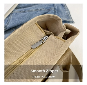 Detail of smooth silver metal zipper on khaki canvas tote bag with textile handles