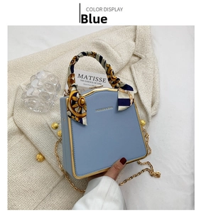 Close-up of light blue mini box bag with gold metal frame and decorative silk handle