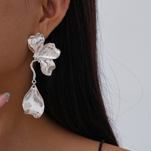 Close-up of oversized silver floral earrings with a hammered metal leaf pendant