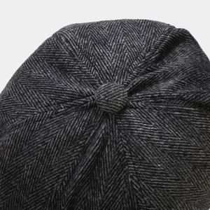 Close-up of dark grey herringbone wool newsboy cap showing top button and stitching detail