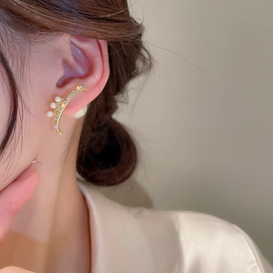 Detail view of curved gold pearl earrings with sparkling rhinestones on the earlobe