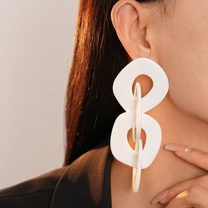 Gros plan de boucles d'oreilles blanches géométriques en chaîne sur un modèle au soleil