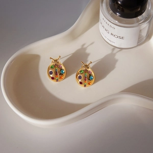 Detail of ladybug stud earrings with multicolor crystals on a white ceramic tray