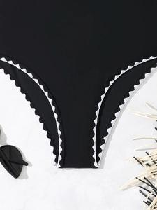 Detailed view of black bikini bottoms with elegant white scalloped edges on flat lay
