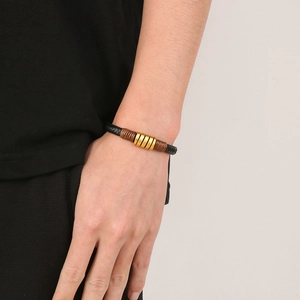 Detail of men's woven leather bracelet with golden rings and brown thread accents