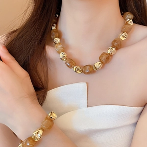 Close-up of amber resin and gold metal bead bracelet set worn by a model on white outfit