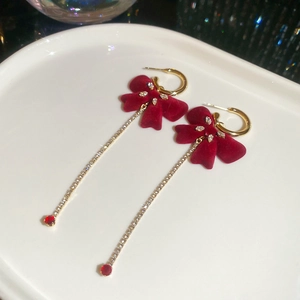 Detailed macro shot of long burgundy velvet bow earrings with sparkling tassel chains