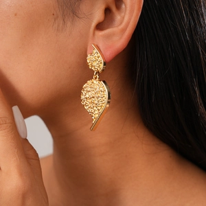 Detailed view of gold leaf-shaped earrings with textured metallic finish on model