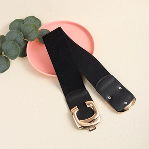 Elastic black waist belt for women with geometric gold buckle on light pink tray