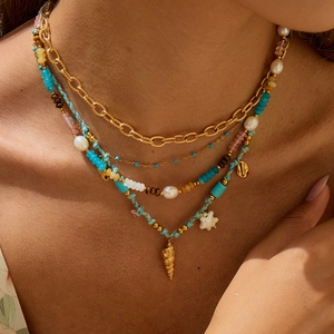 Détail d'un collier multicouche en acier inoxydable doré avec pierres et pendentifs marins