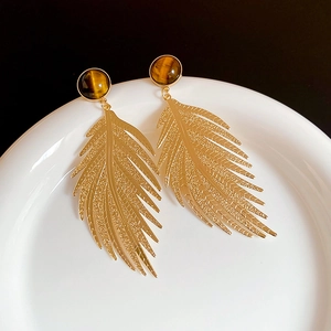 Detailed view of vintage gold leaf earrings featuring tiger eye stone on white ceramic