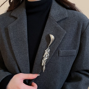 Detail of silver metallic geometric tassel brooch on a dark grey wool blazer lapel