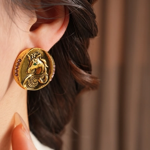 Close-up of vintage gold unicorn earrings with purple crystals on a model