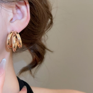 Close-up of triple-layered gold metal hoop earrings worn by a model in warm lighting