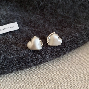 Detail of matte silver heart-shaped hoop earrings with a textured frosted finish
