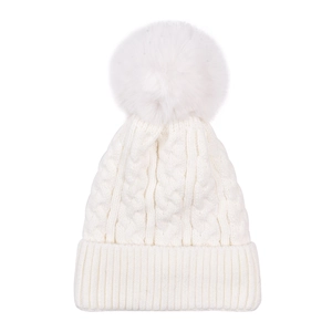 Detail of chunky cable knit white beanie with large faux fur pom-pom and ribbed cuff