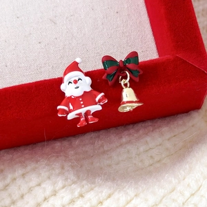 Detailed macro view of asymmetric Santa and bell stud earrings on a red velvet jewelry box