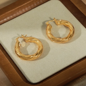 Fashionable golden twisted geometric hoop earrings on a velvet wooden display tray
