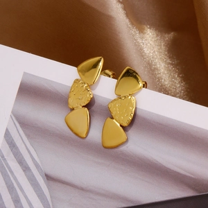Detail of golden triangular earrings with smooth and hammered metal texture surfaces