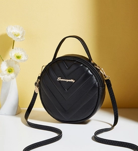 Detail of round black handbag with V-shaped stitching and golden metal logo branding