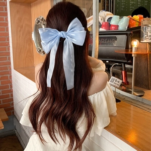 Elegant large light blue tulle bow hair clip with long ribbons on wavy brown hair