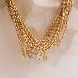 Detailed view of layered gold bead necklaces with crystal-encrusted alphabet pendants