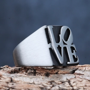 Macro shot of stainless steel LOVE ring with brushed finish on a natural wood base