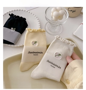 Detail of cream-colored cotton crew socks with ruffled edges and floral embroidery