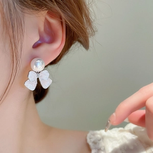 Close-up of pearl bow earrings with micro-set diamonds worn on a female model