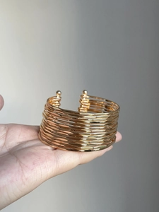Detail of layered gold open cuff bracelet with polished multi-row metallic texture