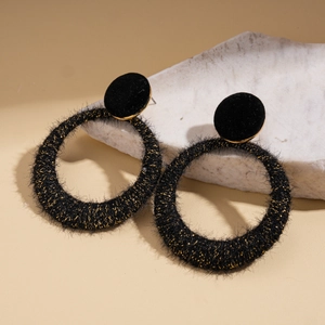 Detailed view of black flocked hoop earrings with gold glitter on neutral stone props