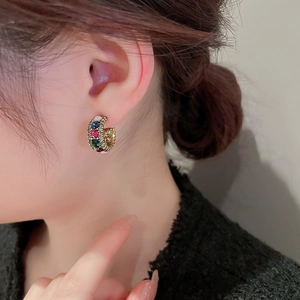 Close-up of vintage C-shaped gold earrings with colorful rhinestones on a female model