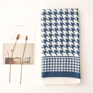 Detailed flat lay of houndstooth scarf with blue border beside minimalist decor items