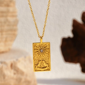 Gold rectangular tarot pendant necklace with sun relief and crystal on stone background