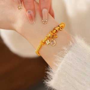Detail of 24k gold plated bracelet with clover charm and oval gemstone on wrist