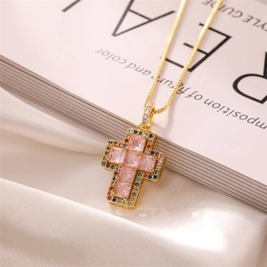 Detail of gold cross pendant with pink square gemstone and colored zircons on white silk