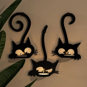 Tre portacandele da parete a forma di gatto in metallo nero con candele accese sul muro